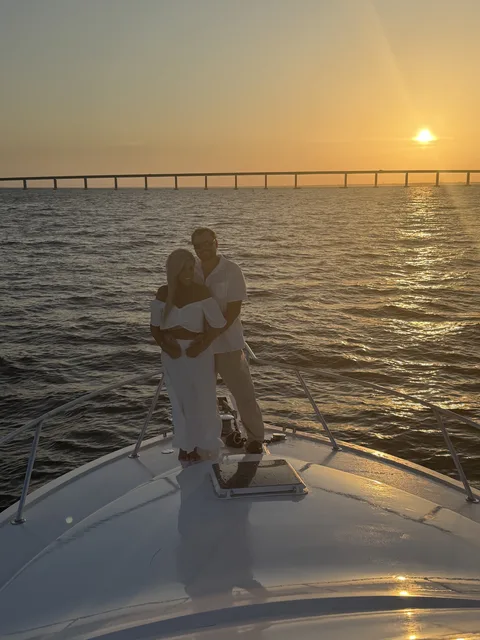 A couple embracing on the bow at sunset with the Destin bridge silhouetted behind them