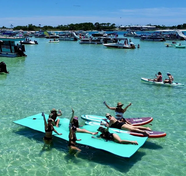 Friends posing on a floating mat surrounded by paddleboards at the crowded Crab Island sandbar in Destin