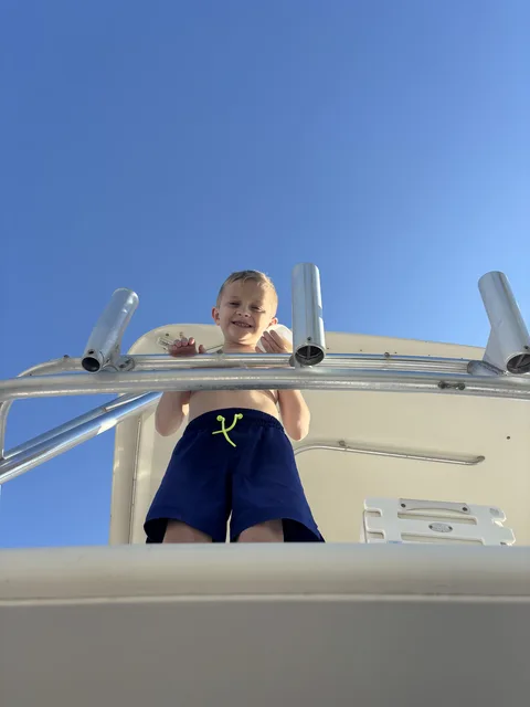 A young boy smiling up at the camera from the deck of a Destin charter boat under a clear blue sky