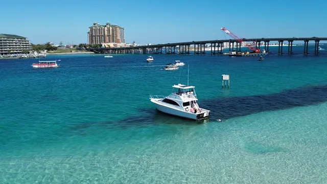 Aerial view of a sportfishing boat crossing the East Pass with the Destin bridge and harbor beyond