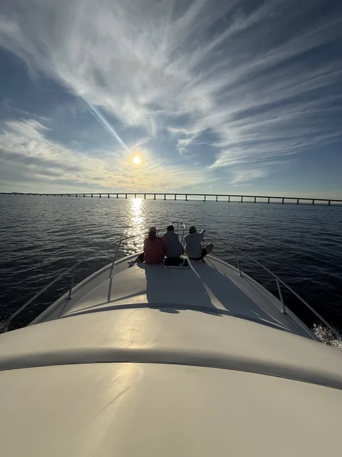 Guests silhouetted on the bow watching the sun set over the Destin bridge