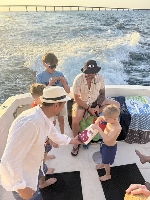 Family sharing snacks on the bow at sunset with the Destin bridge in the background