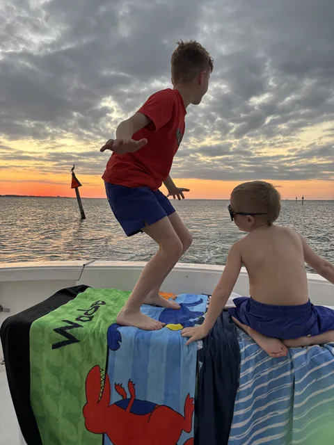 Two kids playing and laughing on the bow of a Destin charter boat as the sun sets over the water