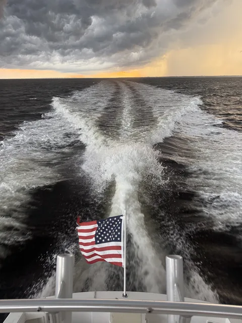 An American flag waving over a Destin charter boat's wake under a dramatic evening sky